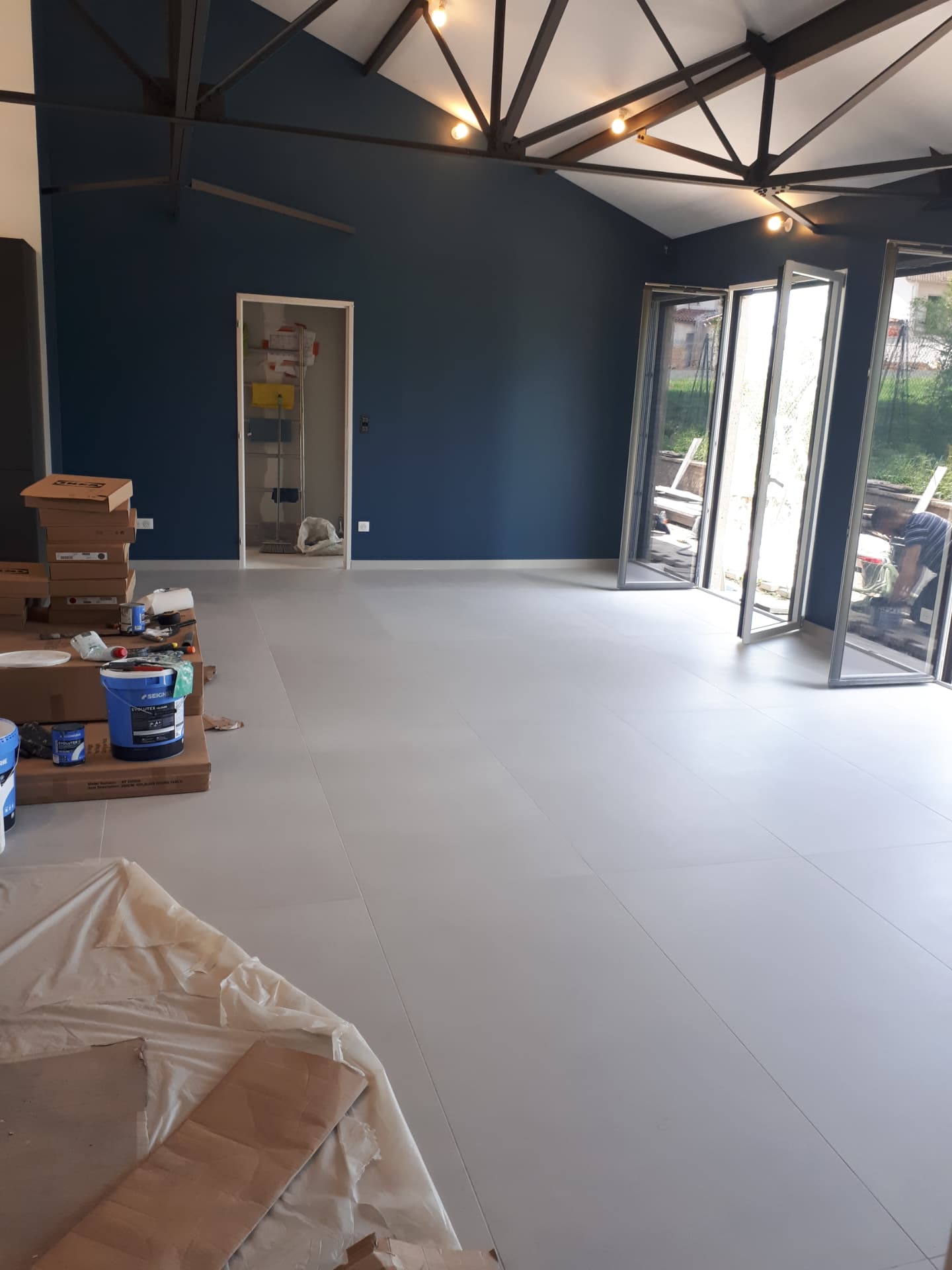 Rénovation d’intérieur en cours — sol carrelé clair, murs bleu profond et baie vitrée